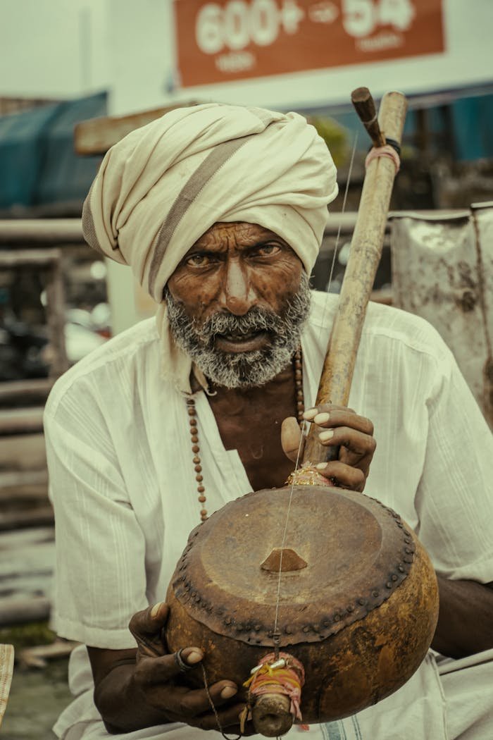 Indian musician with a turban playing a traditional musical instrument outdoors.