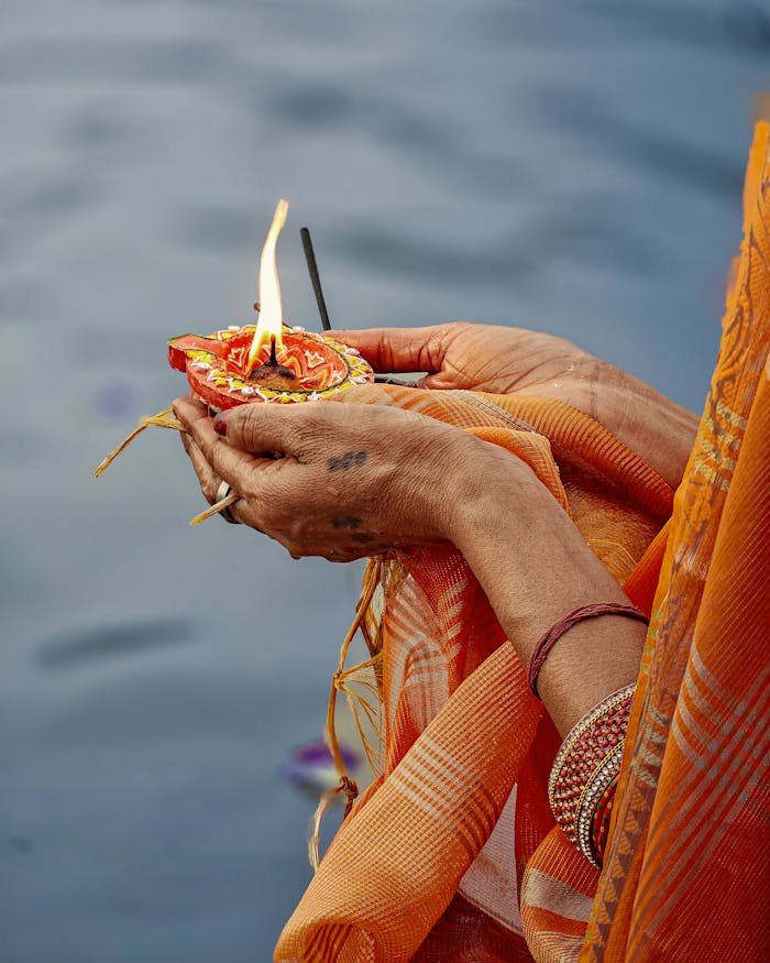 A close-up of hands performing a traditional ritual with a candle on a riverbank.