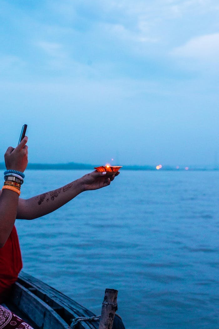 A person on a boat holds a lit candle over calm waters during twilight, capturing a serene and reflective moment.