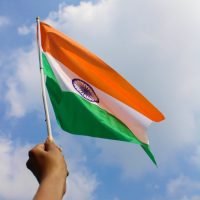 A hand holds the Indian flag aloft against a clear blue sky, symbolizing patriotism.